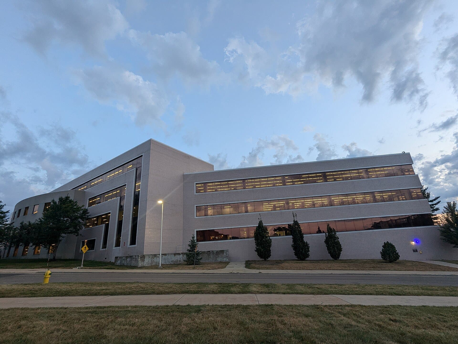 Western Michigan University's Waldo Library, a long modern white building with bands of windows, seen across a lawn and walkway under a blue sky with clouds