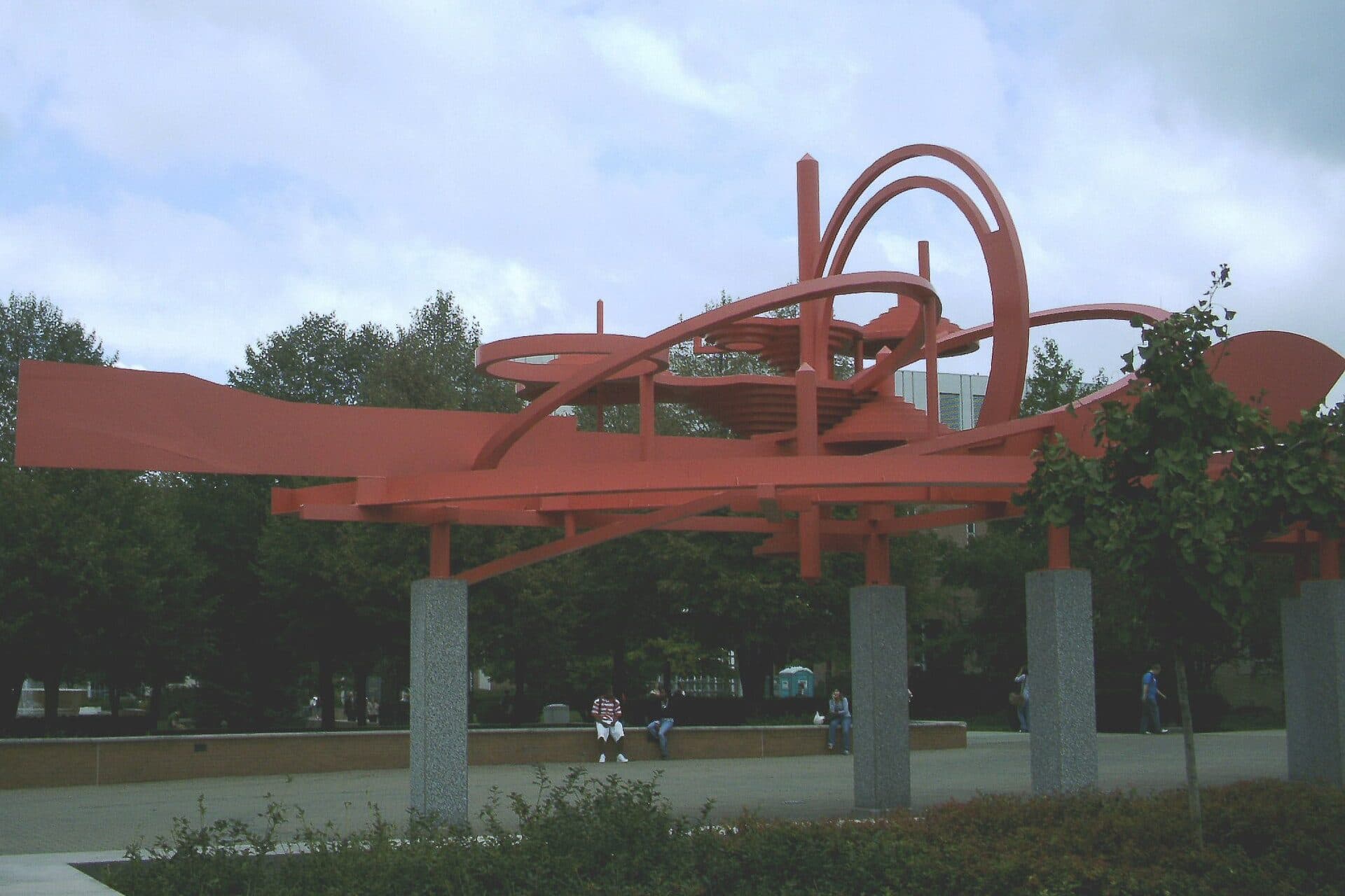 The large red-orange steel Turning Points sculpture on white pillars, set among trees and lawn on the Wright State campus
