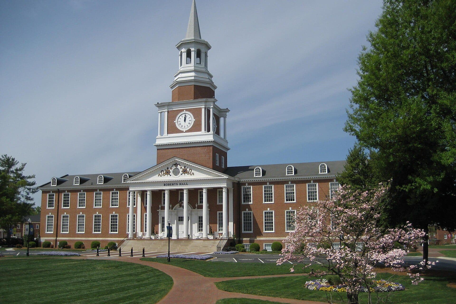 Roberts Hall's clock tower and columned brick facade at High Point University, with a flowering tree in front