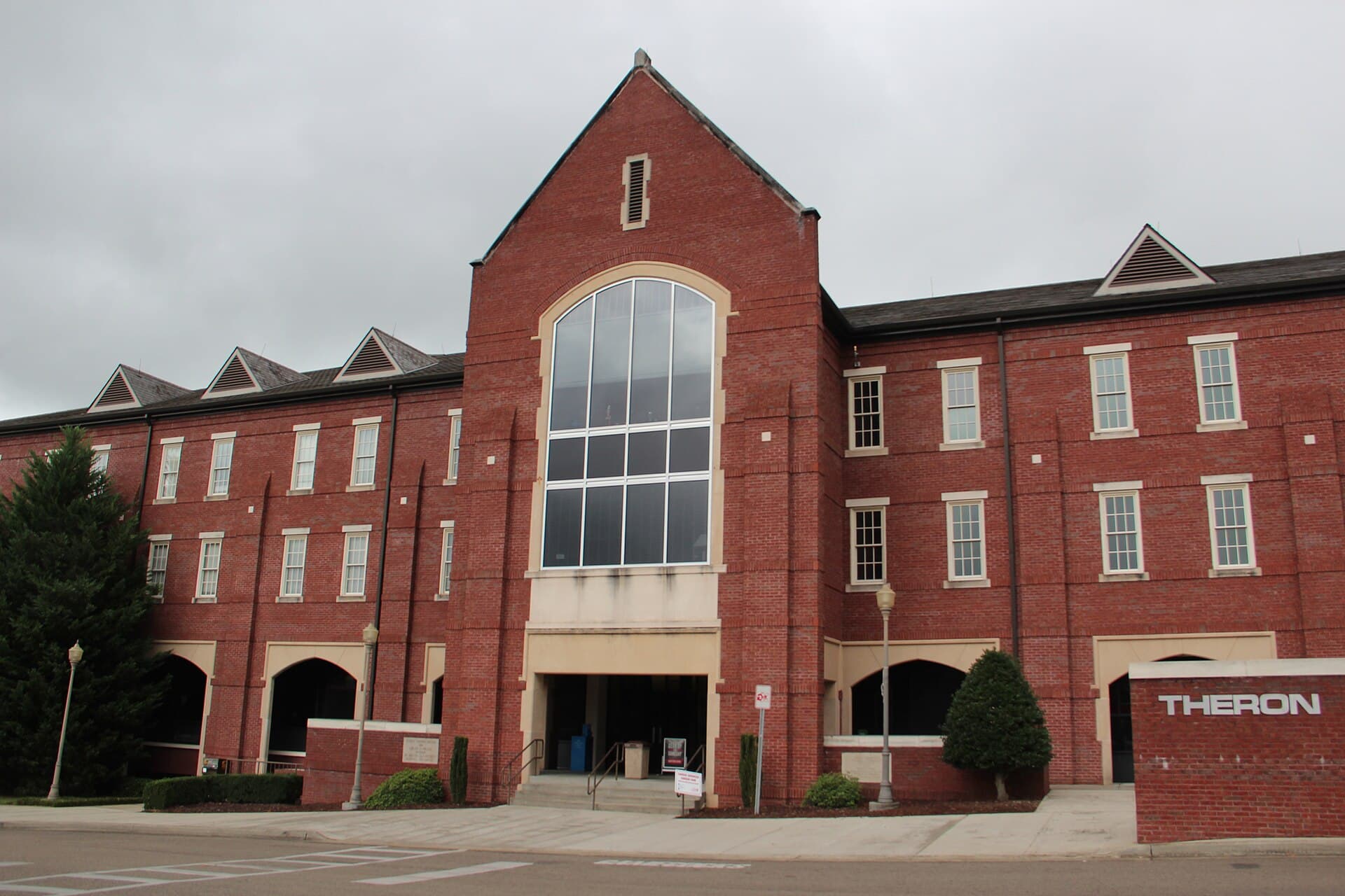 The red-brick Theron Montgomery Building at Jacksonville State University, with a tall arched window over the entrance and the building name on a brick sign out front