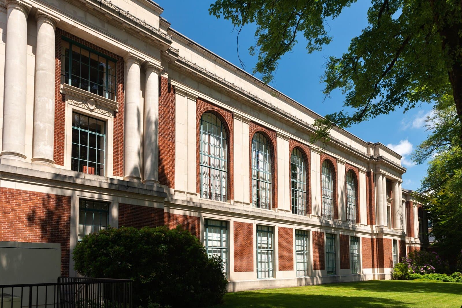 The columned facade and tall arched windows of the Memorial Union, a brick and stone building framed by a large tree and a deep blue sky at Oregon State University