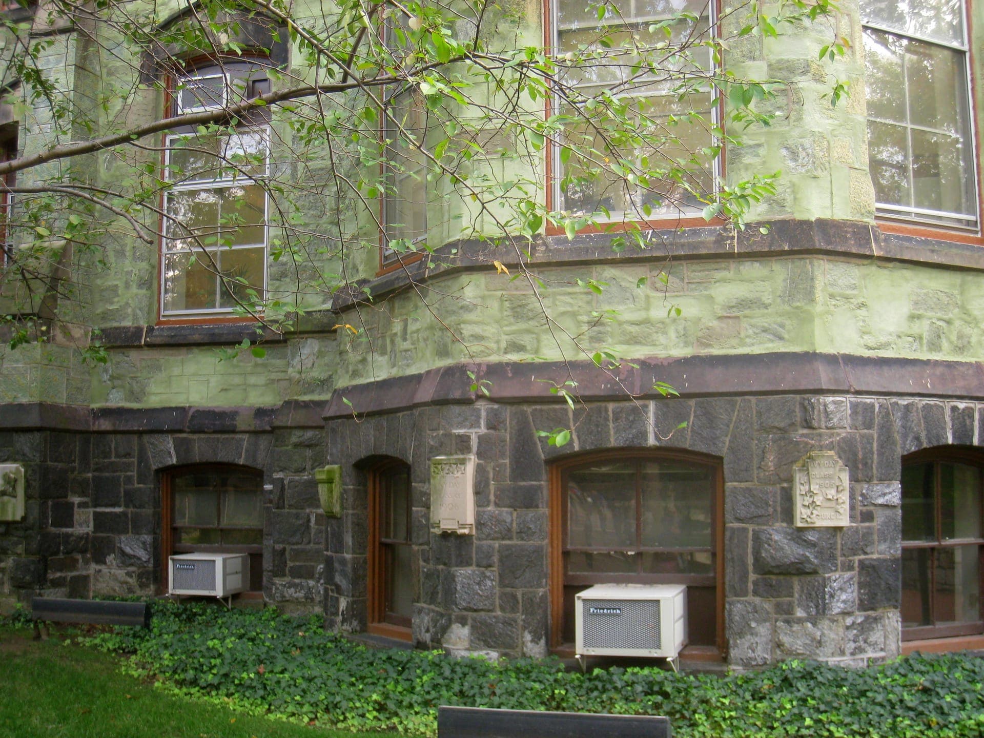 Close view of College Hall at Penn, a green serpentine-stone building with arched windows above a lawn and ivy