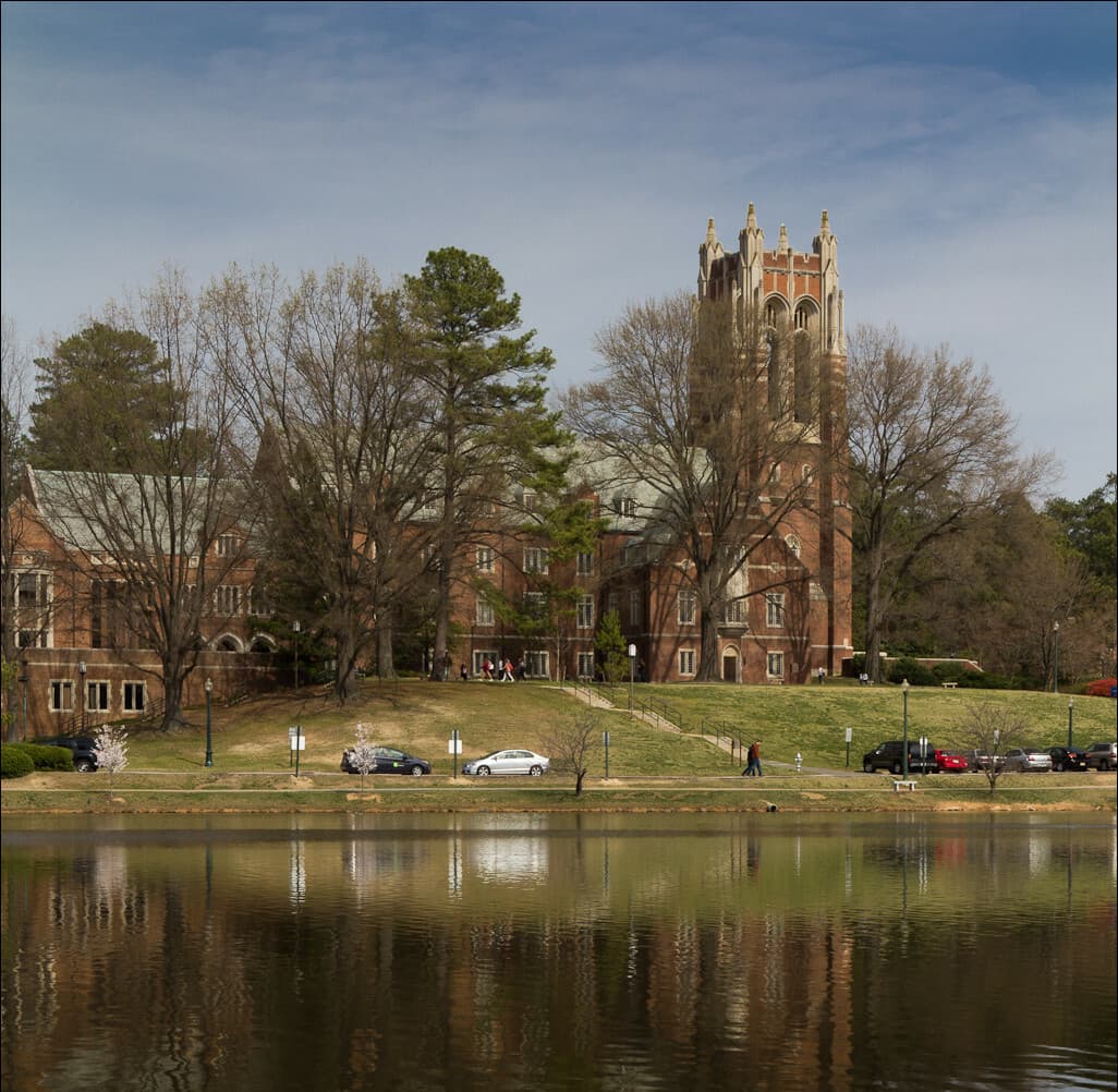 Gothic-style brick buildings and a stone tower at the University of Richmond beyond Westhampton Lake and bare trees