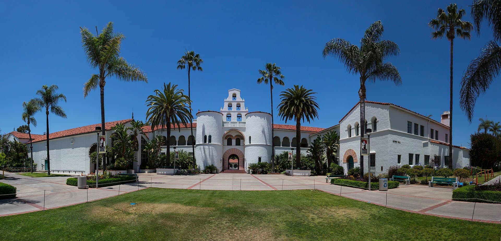 The white Mission Revival towers and arched entrance of Hepner Hall at San Diego State University, framed by palm trees and a lawn under a blue sky