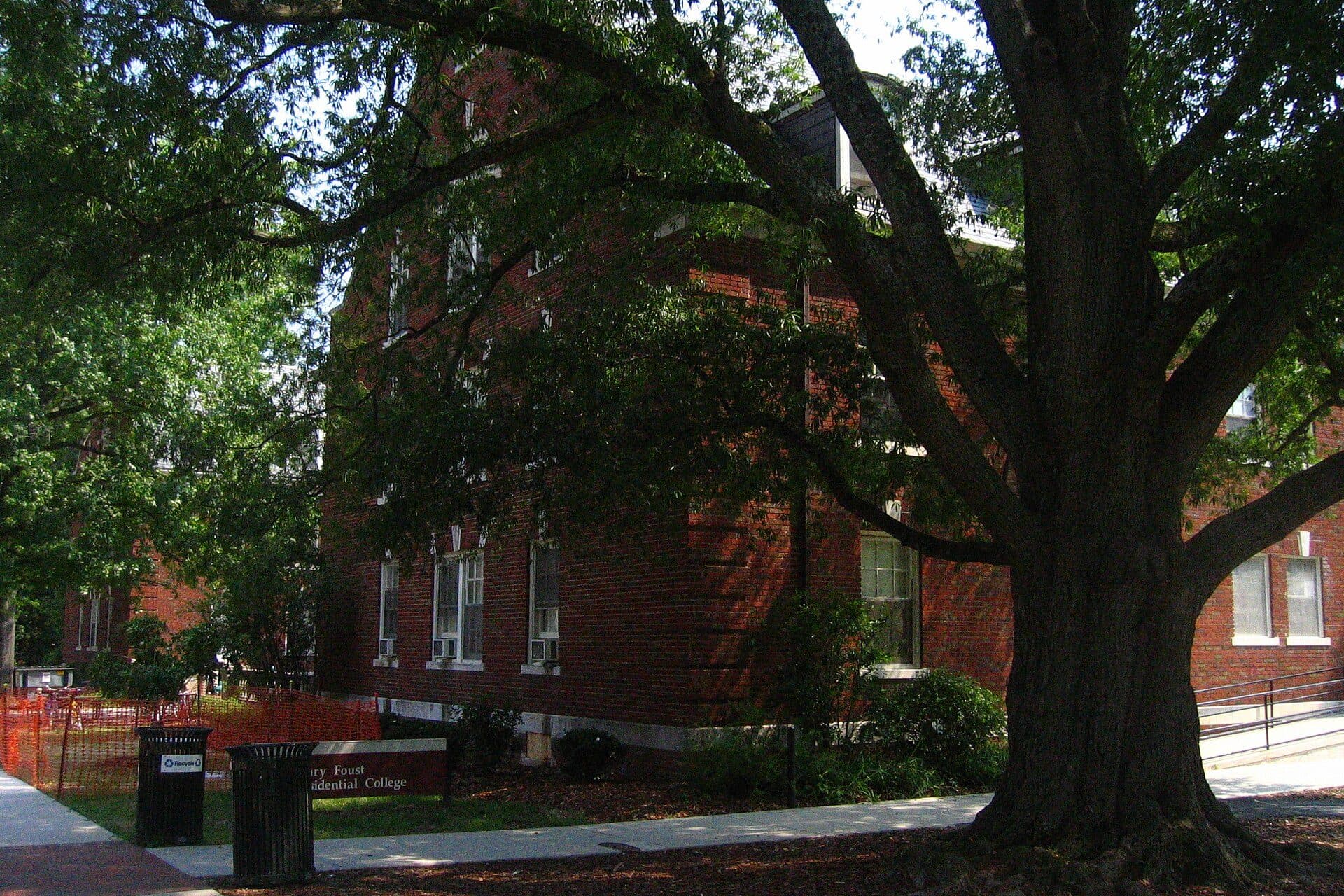 A brick UNCG residence hall behind a large leafy tree