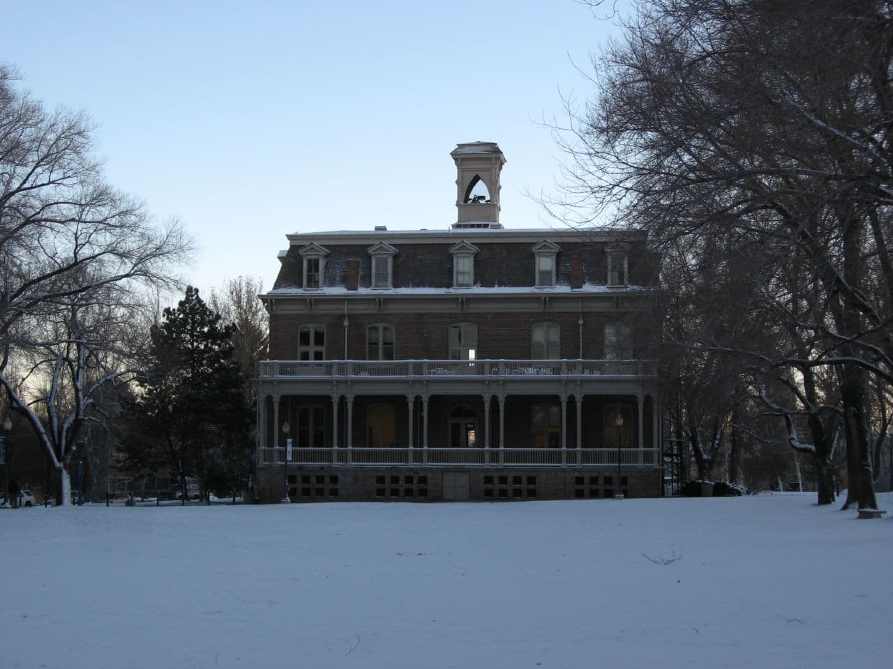 The three-story brick Morrill Hall with a mansard roof, columned porches and a small cupola, seen across a snow-covered quad framed by bare winter trees