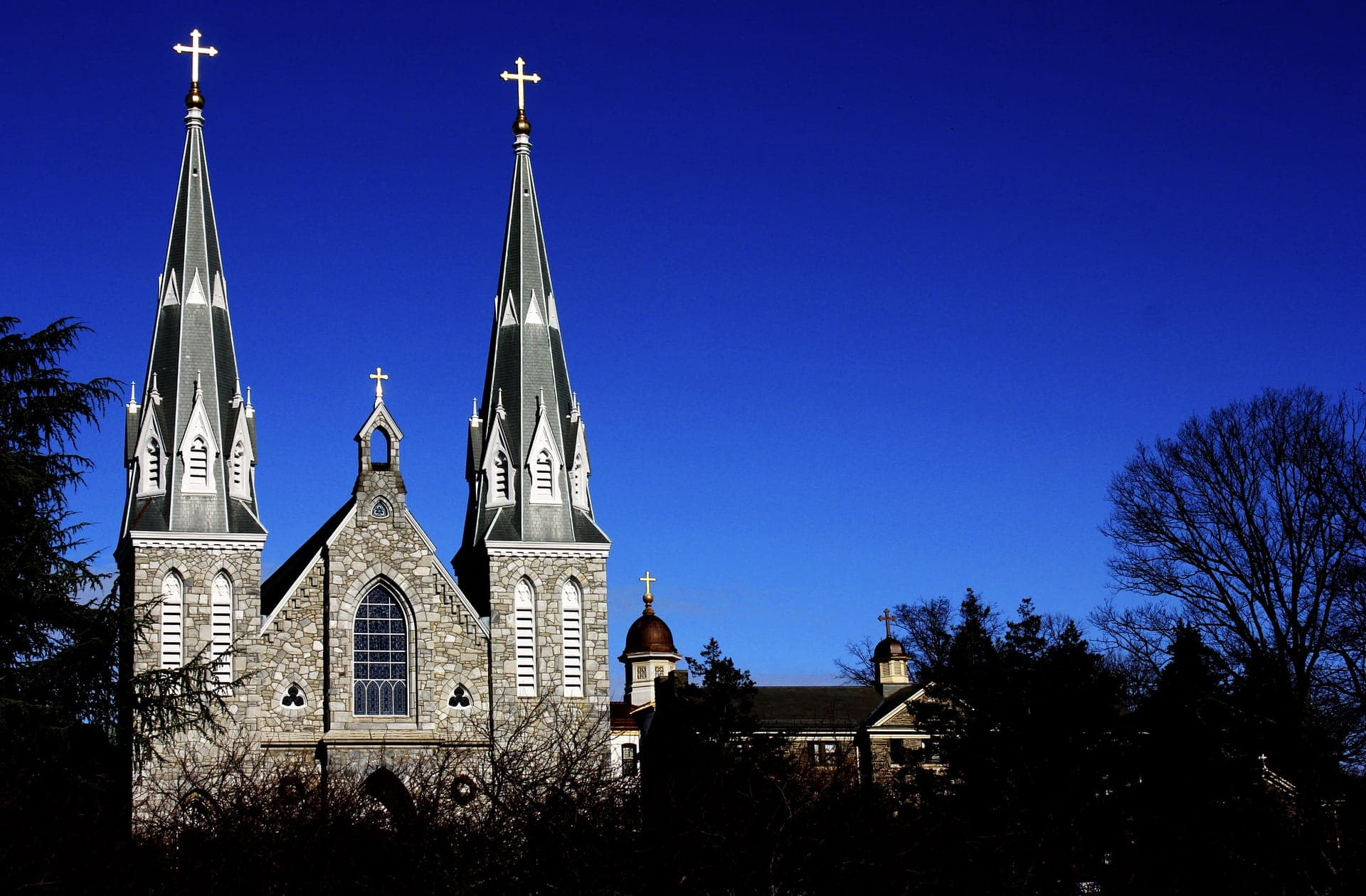 The twin spires of the campus church at Villanova silhouetted against a deep blue sky, with dark trees in front